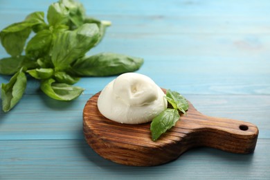 Photo of Delicious burrata cheese with basil on light blue wooden table