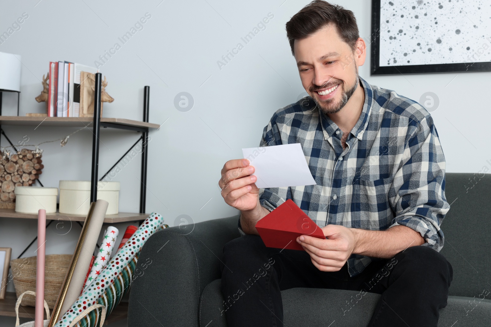 Photo of Happy man reading greeting card on sofa in living room