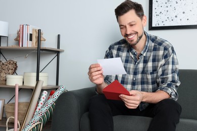 Happy man reading greeting card on sofa in living room