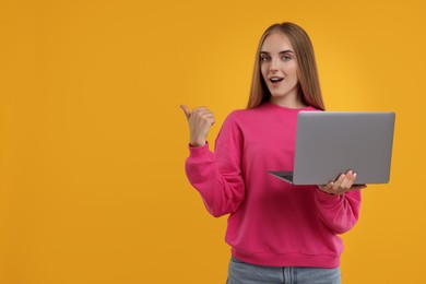 Photo of Special promotion. Young woman with laptop pointing at something on orange background, space for text
