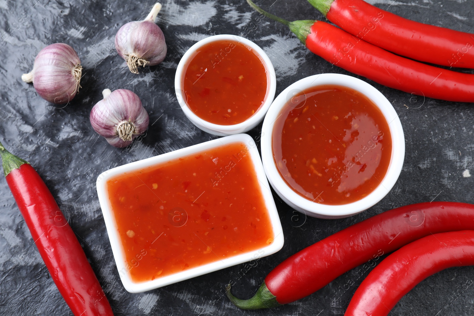 Photo of Spicy chili sauce, peppers and garlic on black textured table, flat lay