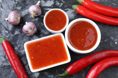 Photo of Spicy chili sauce, peppers and garlic on black textured table, flat lay