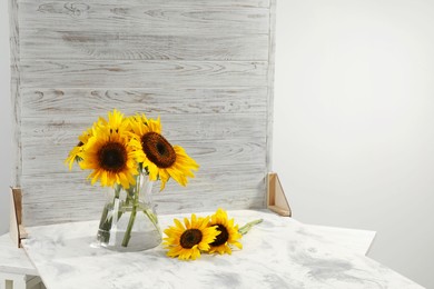 Photo of Glass vase with beautiful sunflowers and double-sided backdrop on table in photo studio