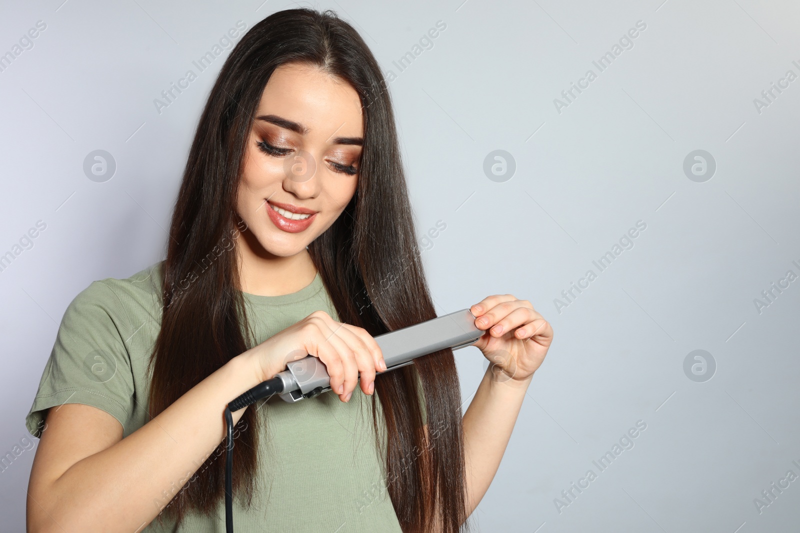 Photo of Happy woman using hair iron on grey background. Space for text