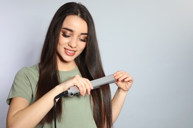 Happy woman using hair iron on grey background. Space for text