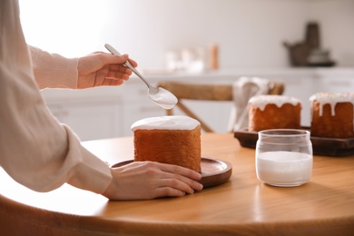 Photo of Young woman decorating traditional Easter cake with glaze in kitchen, closeup