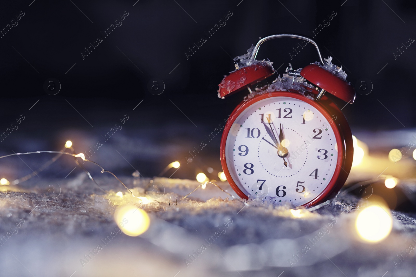 Photo of Alarm clock and Christmas lights on white snow outdoors, space for text. Midnight countdown