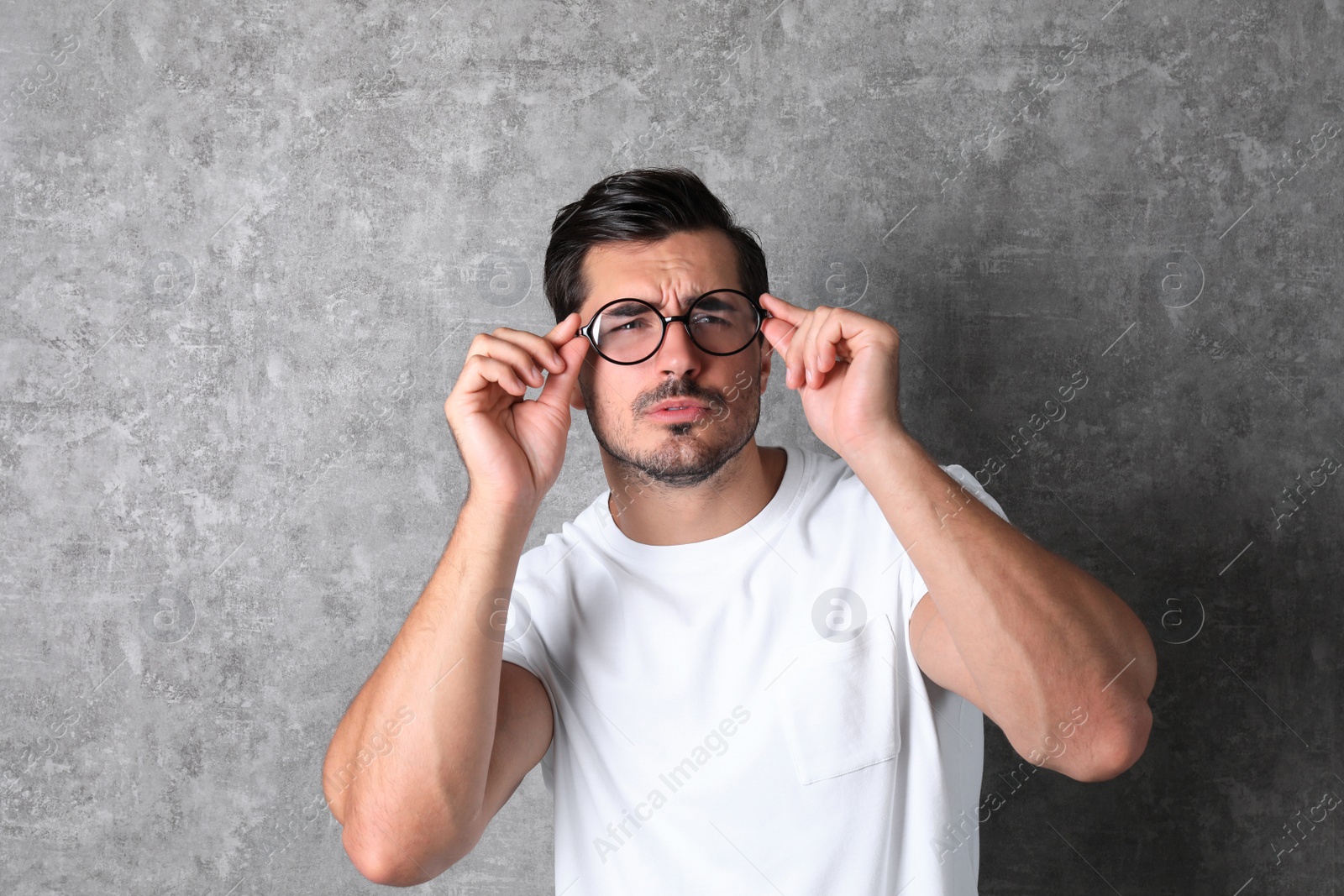 Photo of Young man with vision problem wearing glasses on grey background