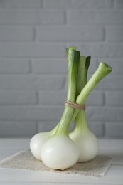 Photo of Bunch of fresh green spring onions on white wooden table against brick wall, closeup