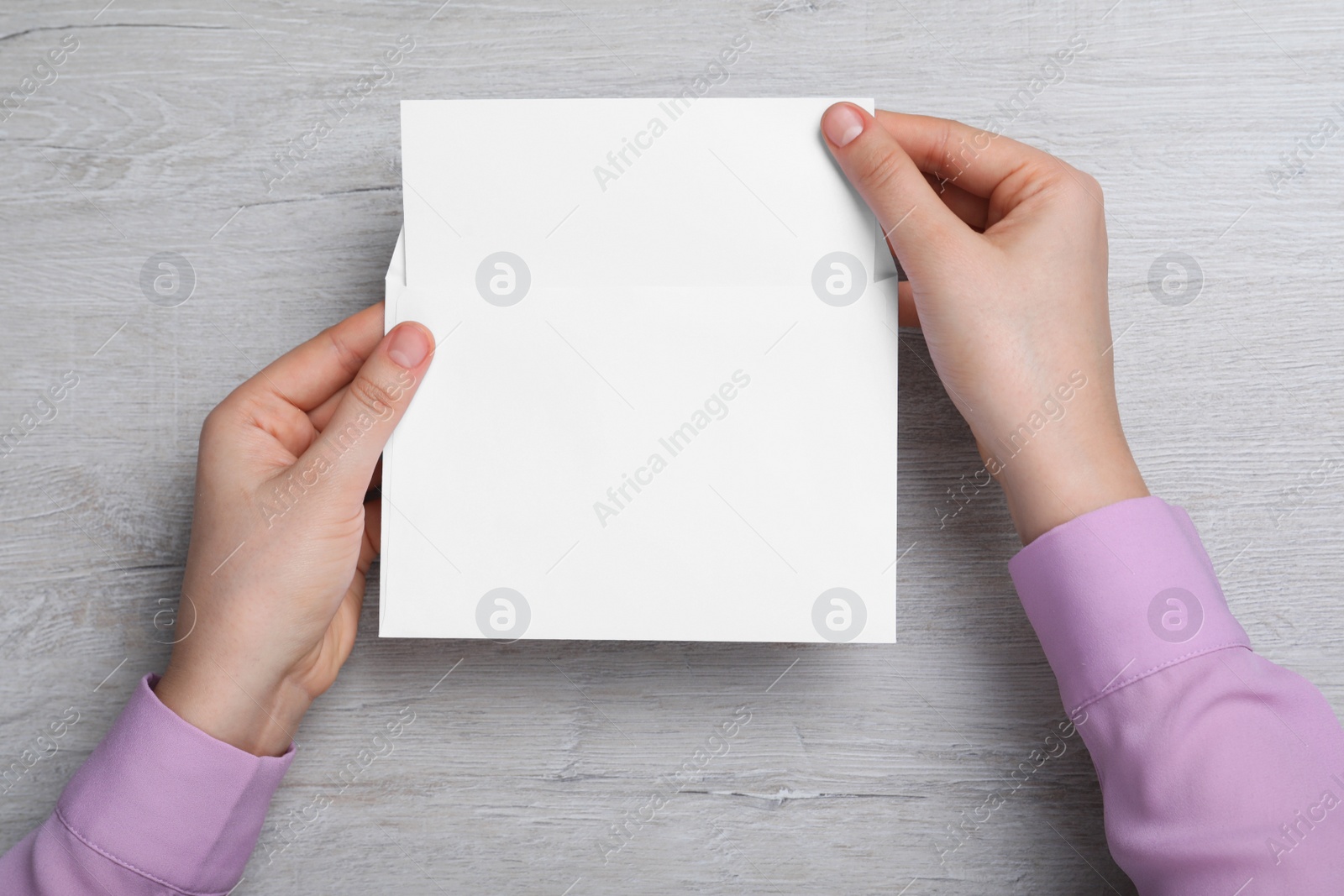 Photo of Woman taking card out of envelope at wooden table, top view