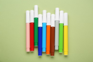 Different colorful markers on light green background, flat lay