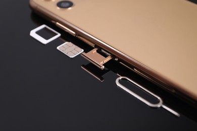Photo of SIM card, smartphone and ejector on black background, closeup