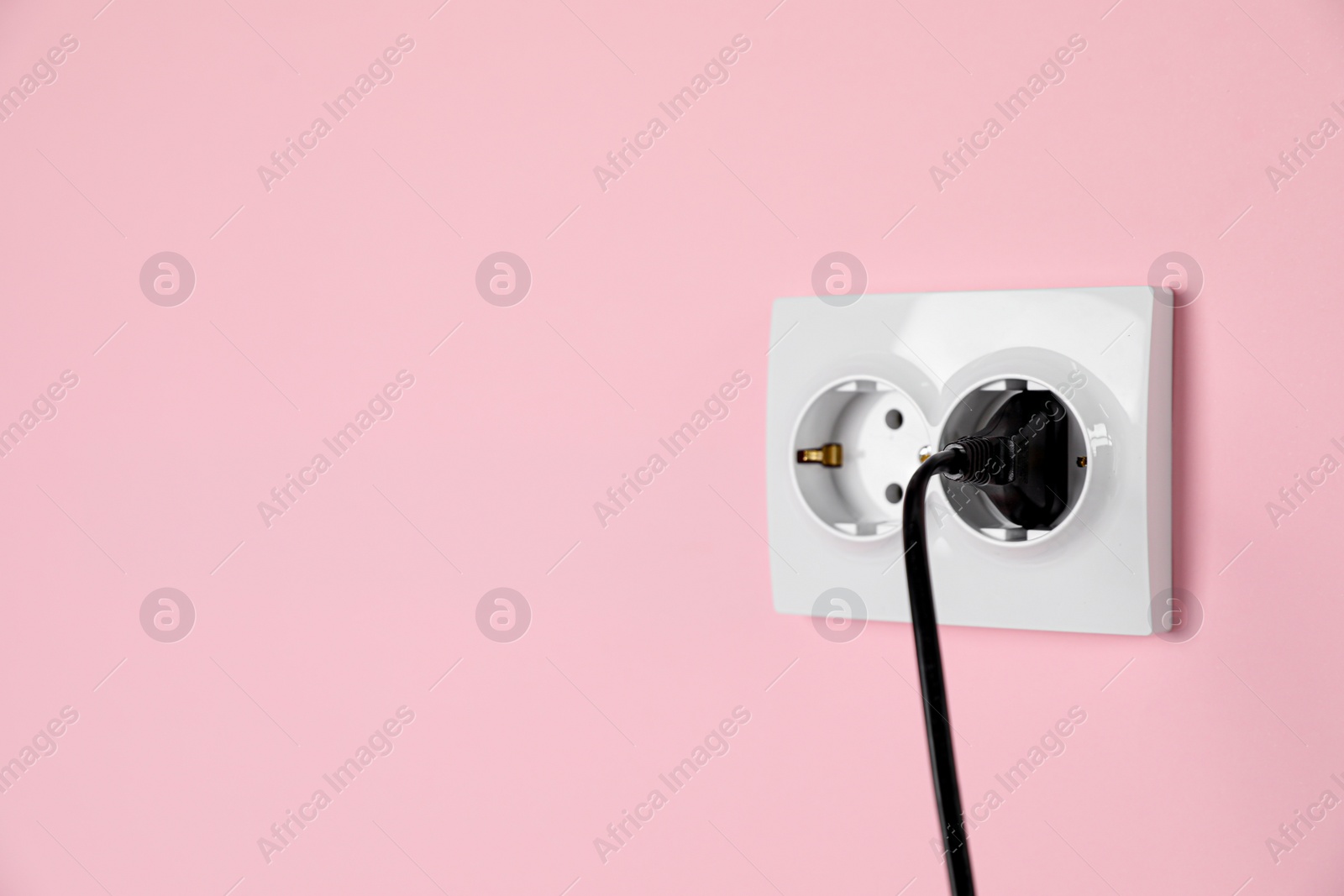 Photo of Power sockets with inserted plug on pink wall, space for text. Electrical supply