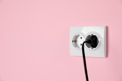 Power sockets with inserted plug on pink wall, space for text. Electrical supply