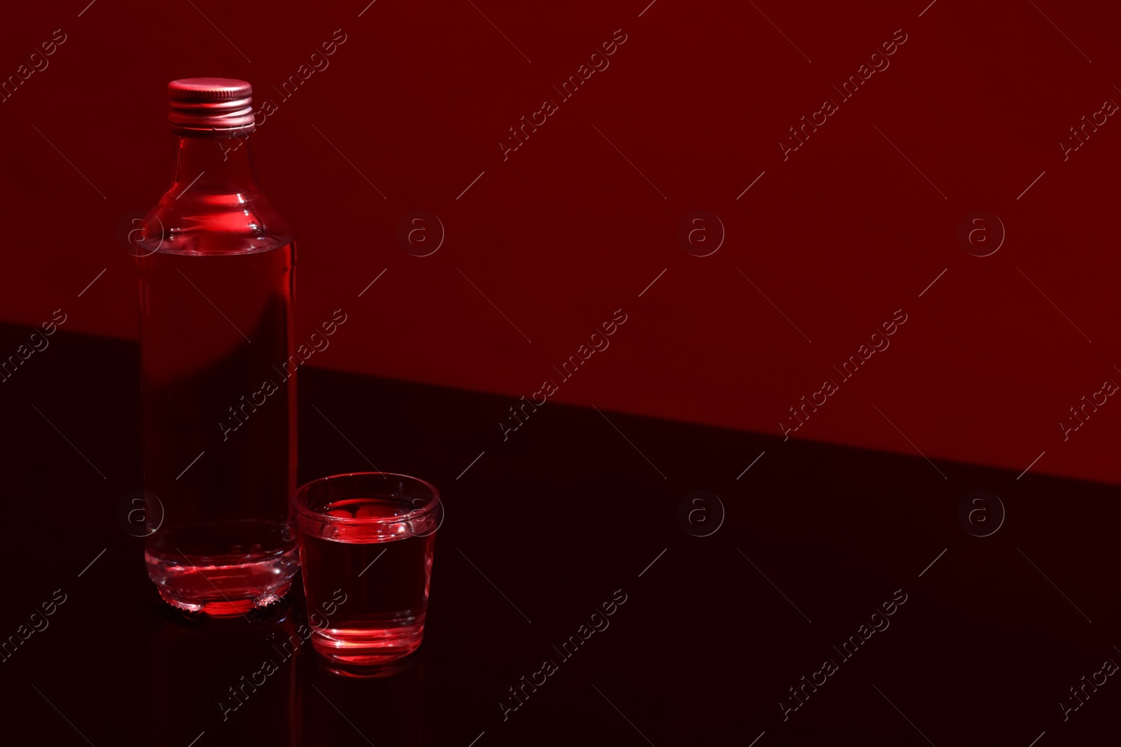 Photo of Bottle and glass with vodka on table against red background, space for text