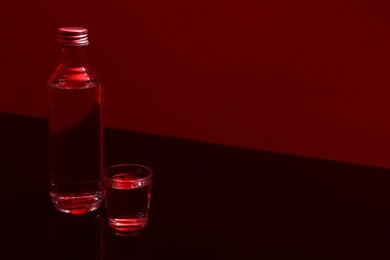 Photo of Bottle and glass with vodka on table against red background, space for text
