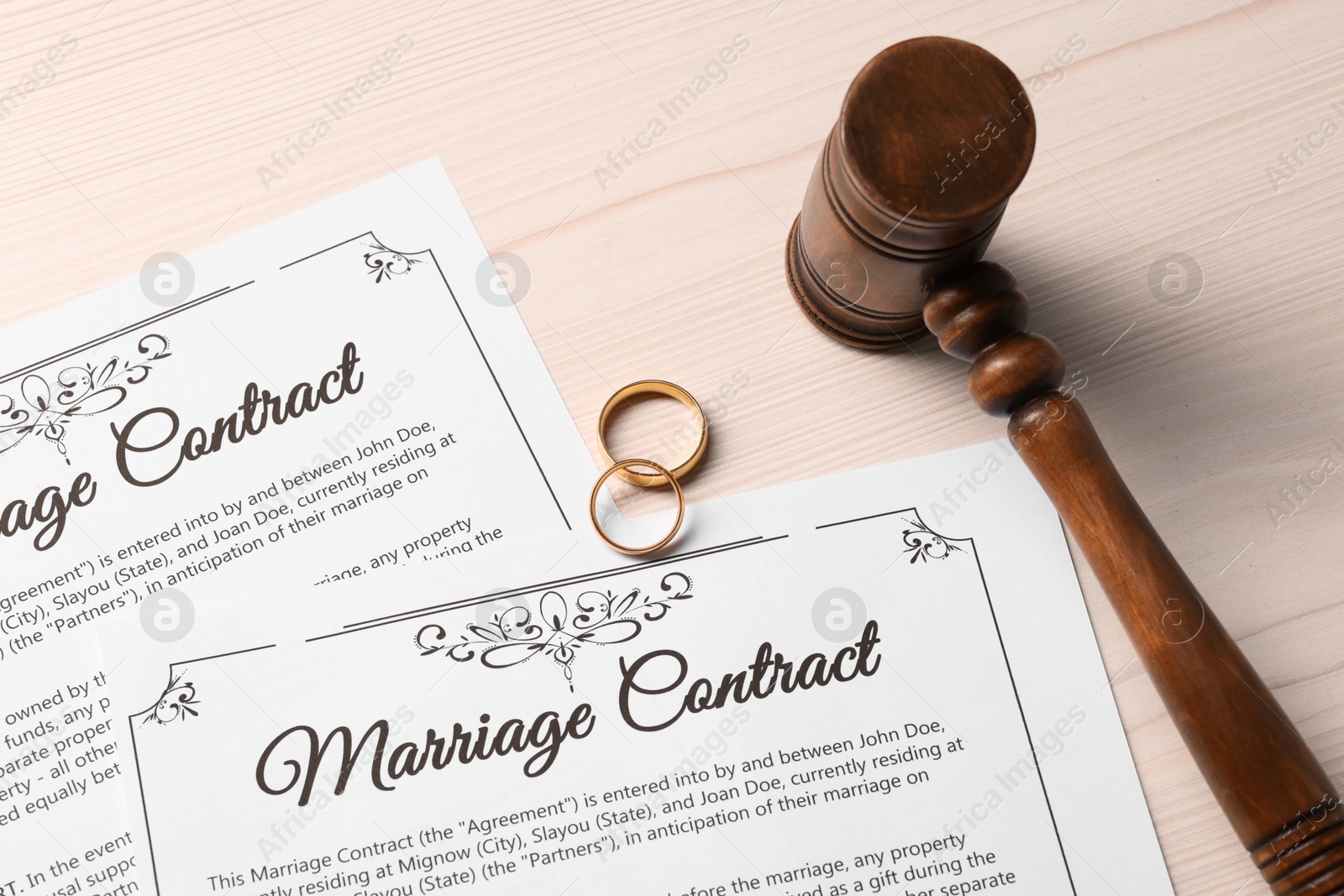 Photo of Marriage contracts, gold rings and gavel on light wooden table, top view