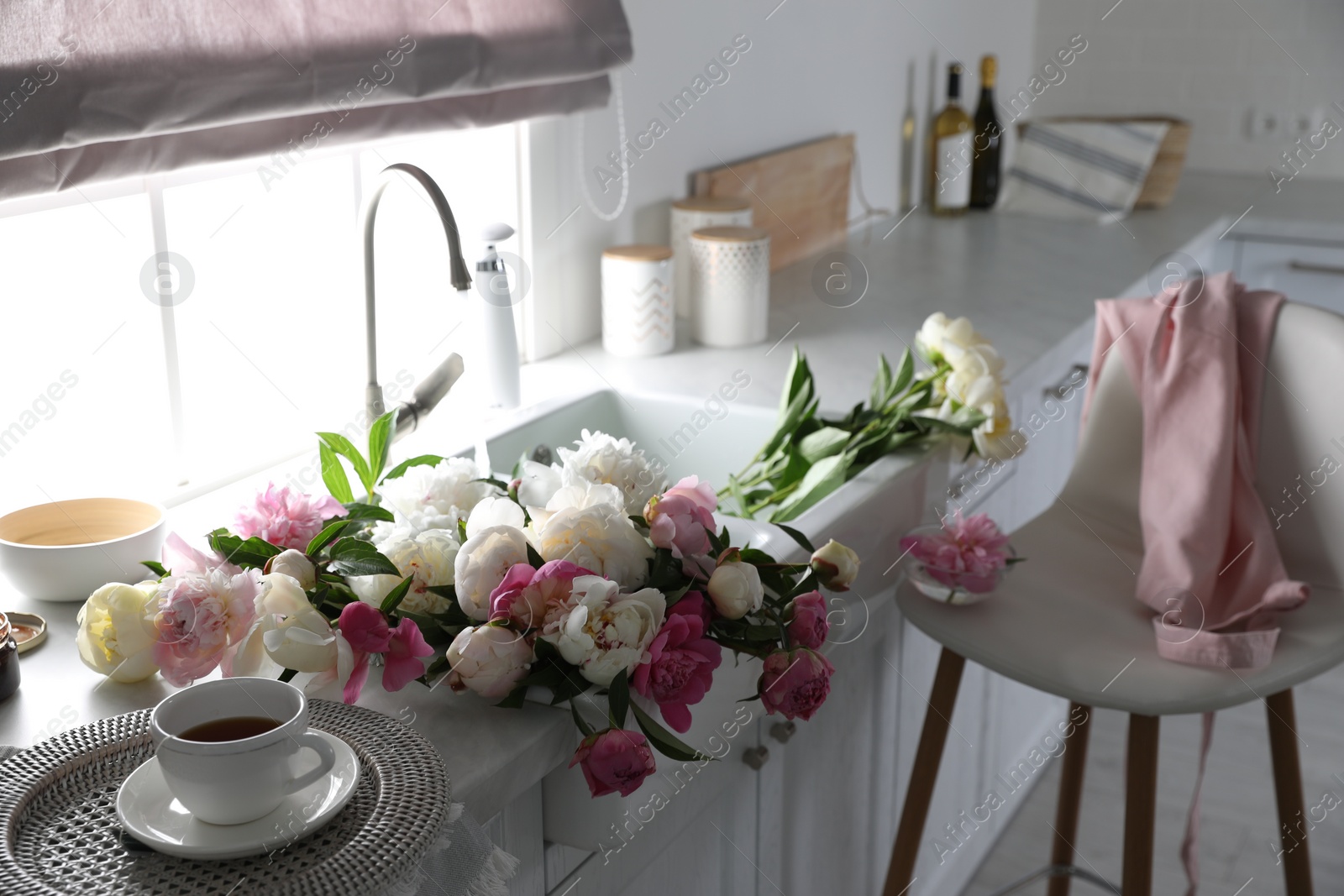 Photo of Beautiful peonies and cup of tea on kitchen counter