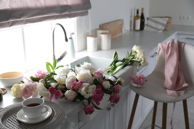 Photo of Beautiful peonies and cup of tea on kitchen counter