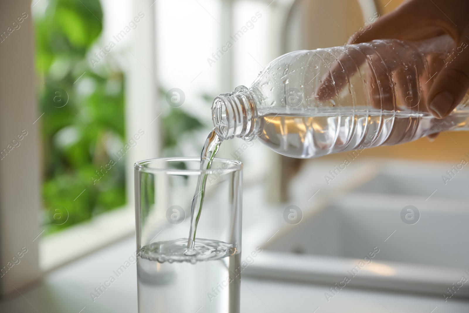 Photo of Woman pouring water from bottle into glass in kitchen, closeup