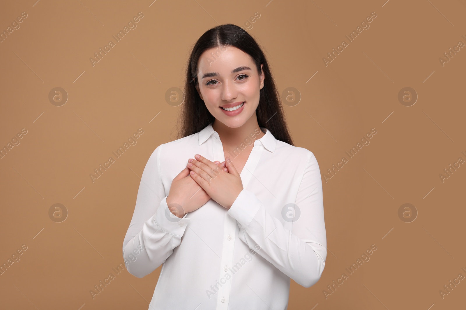 Photo of Thank you gesture. Beautiful grateful woman with hands on chest against brown background