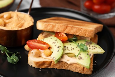 Photo of Delicious sandwich with hummus and vegetables on black plate, closeup