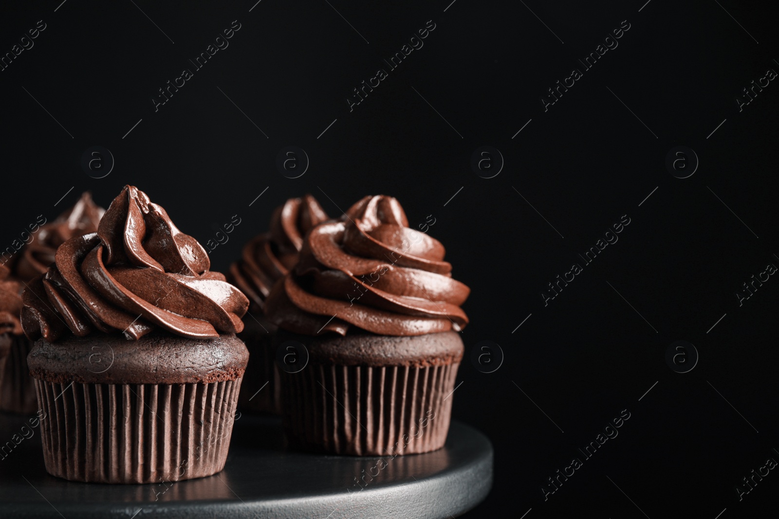Photo of Delicious chocolate cupcakes with cream on dessert stand against black background, closeup. Space for text