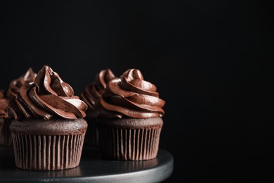 Delicious chocolate cupcakes with cream on dessert stand against black background, closeup. Space for text