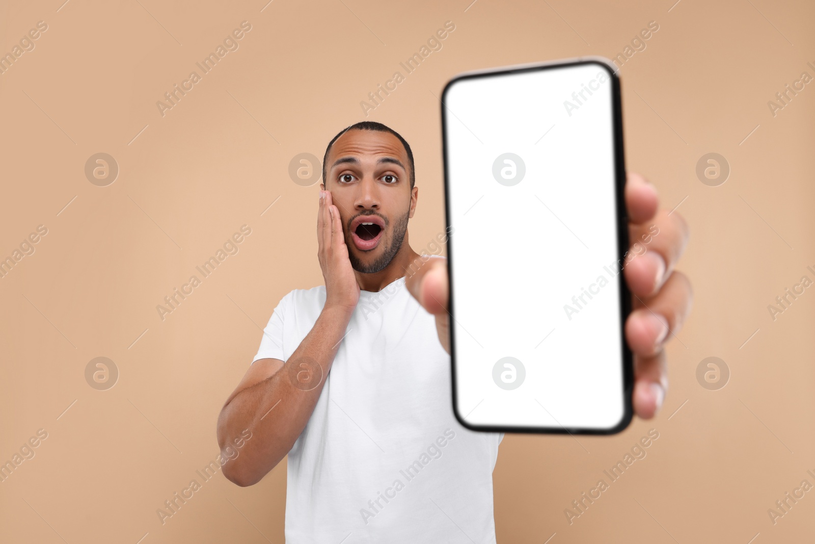 Photo of Surprised man showing smartphone in hand on beige background