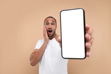 Surprised man showing smartphone in hand on beige background