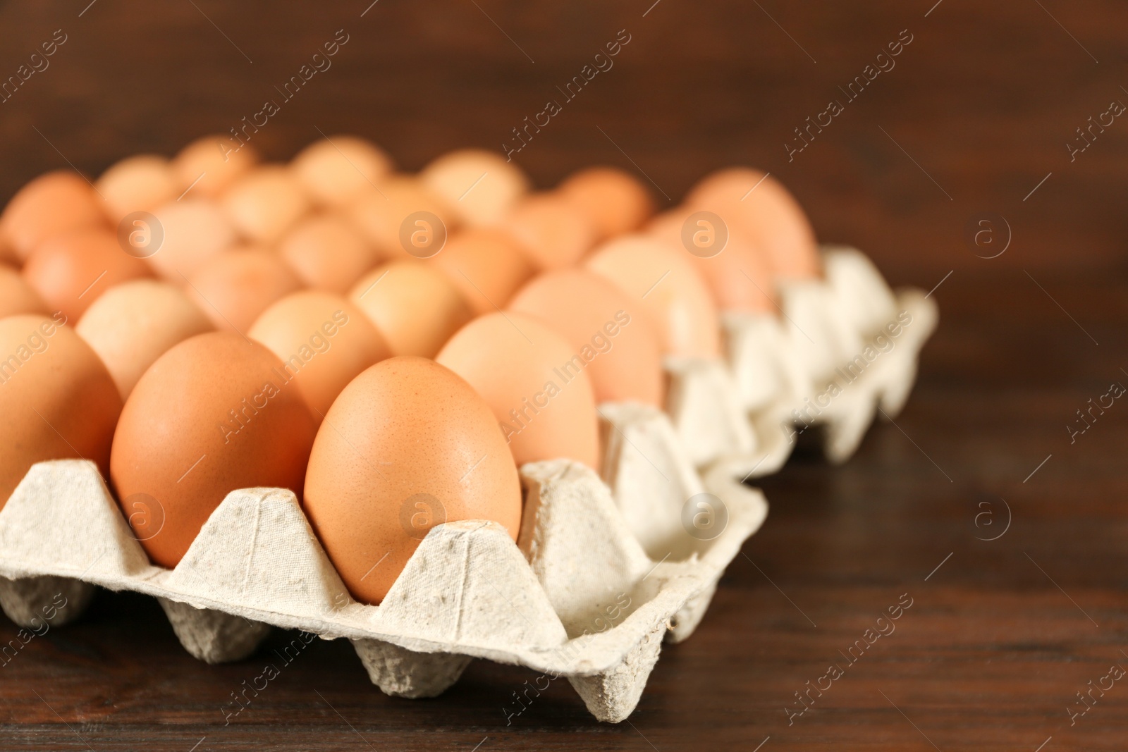 Photo of Raw chicken eggs in carton tray on wooden table, closeup