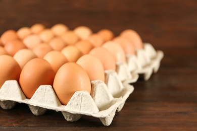 Raw chicken eggs in carton tray on wooden table, closeup