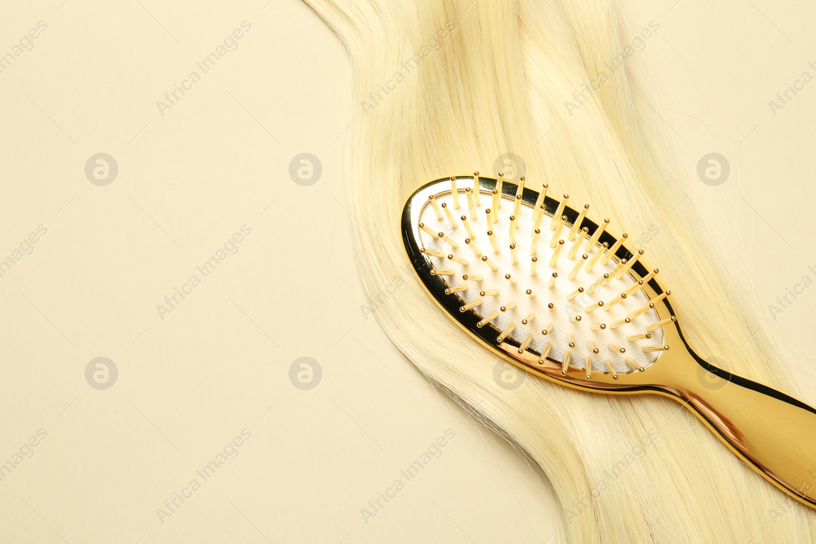 Photo of Stylish brush with blonde hair strand on beige background, top view. Space for text