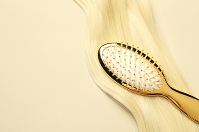 Stylish brush with blonde hair strand on beige background, top view. Space for text