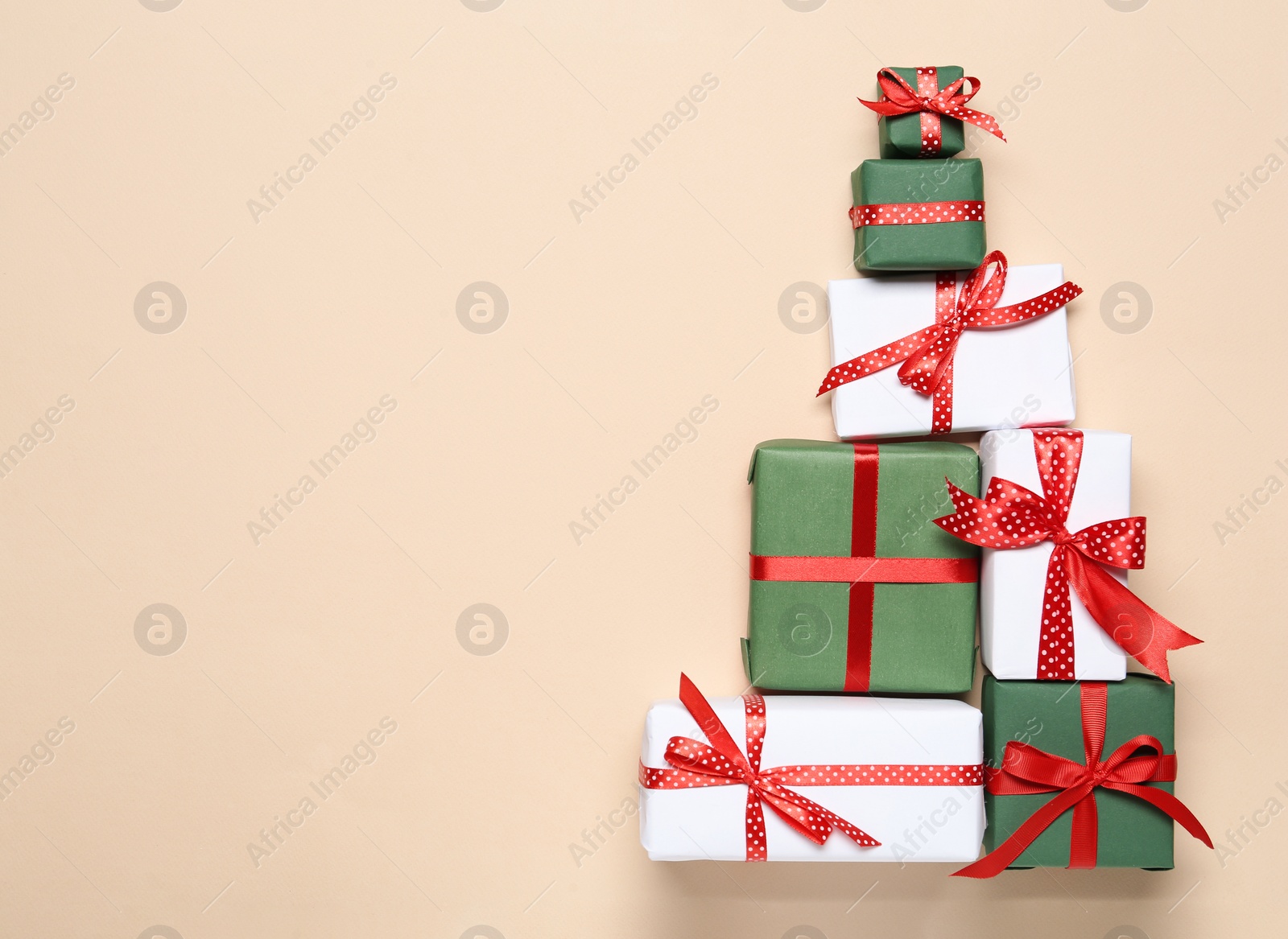 Photo of Christmas tree shape of gift boxes on beige background, flat lay. Space for text