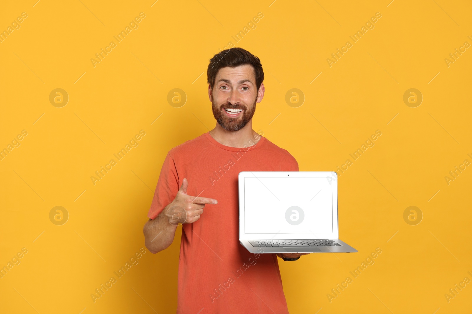 Photo of Handsome man with laptop on orange background