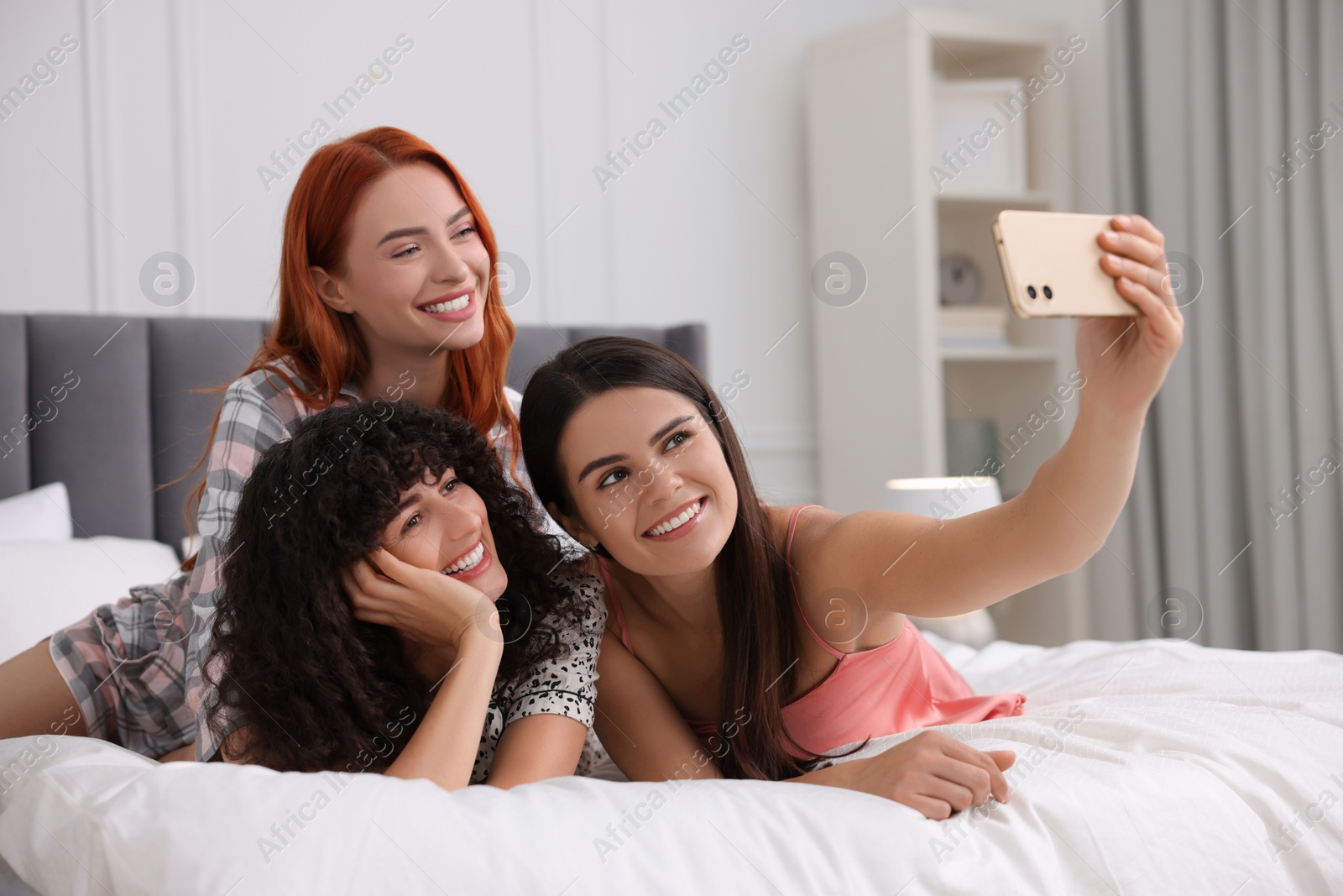 Photo of Happy young friends taking selfie on bed at home