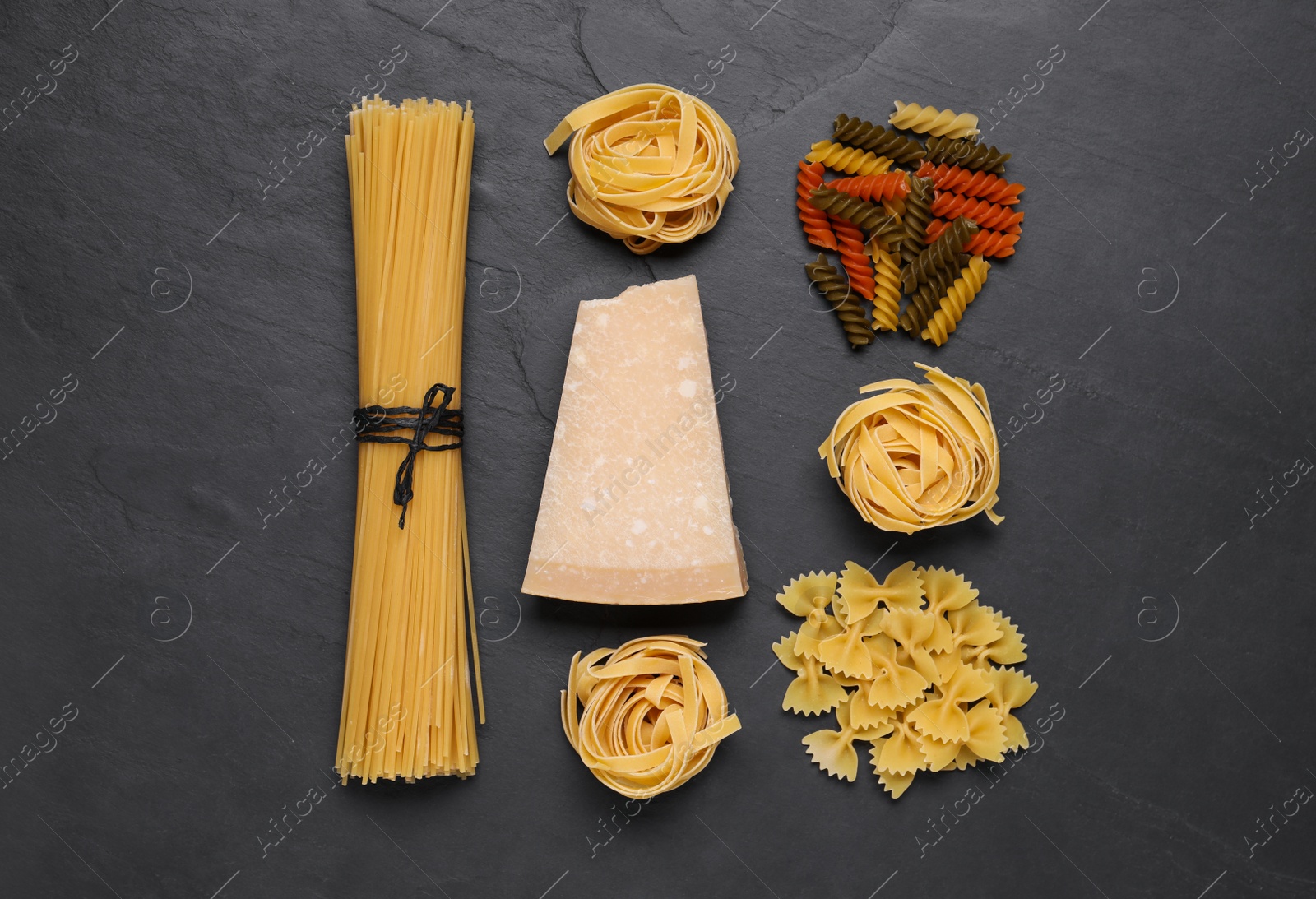 Photo of Different types of pasta and cheese on black table, flat lay