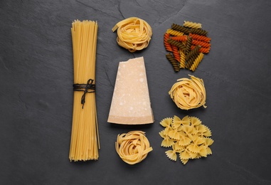 Different types of pasta and cheese on black table, flat lay