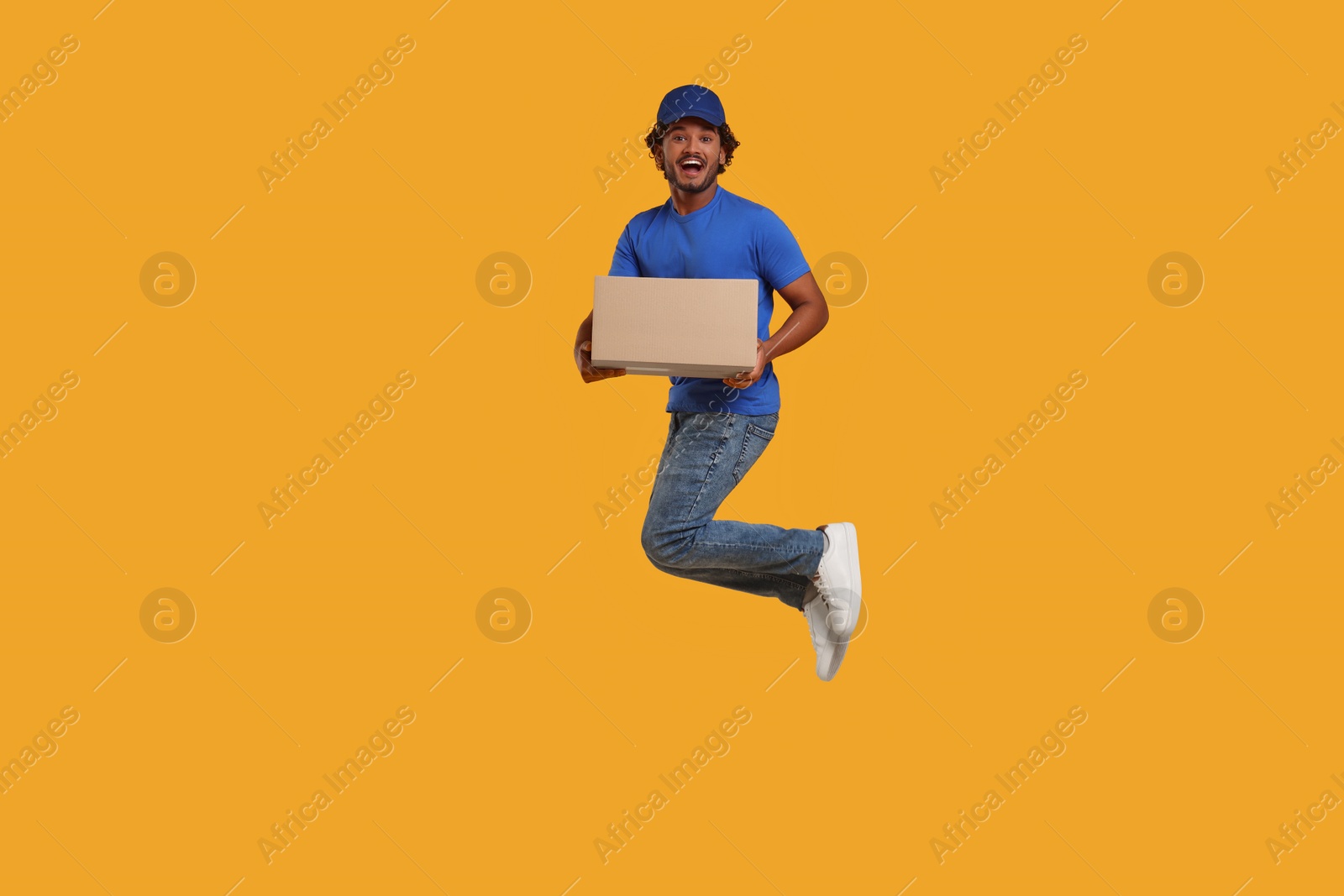 Photo of Happy courier with parcel jumping on orange background