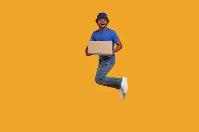 Photo of Happy courier with parcel jumping on orange background