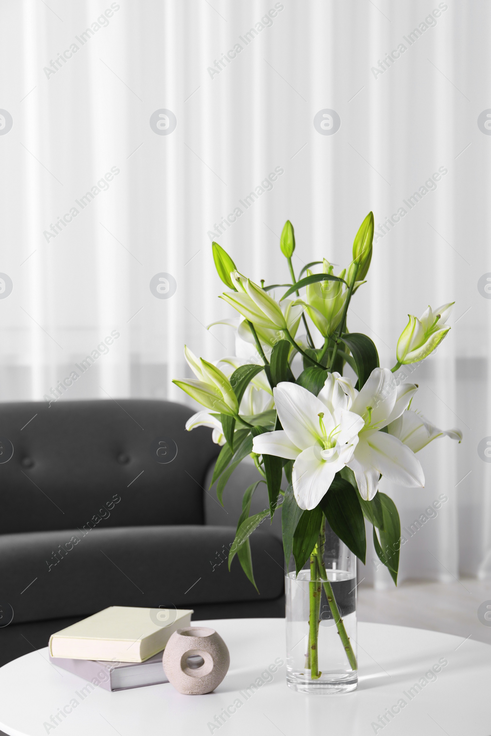 Photo of Beautiful bouquet of lily flowers in glass vase, aromalamp and books on coffee table in living room, space for text