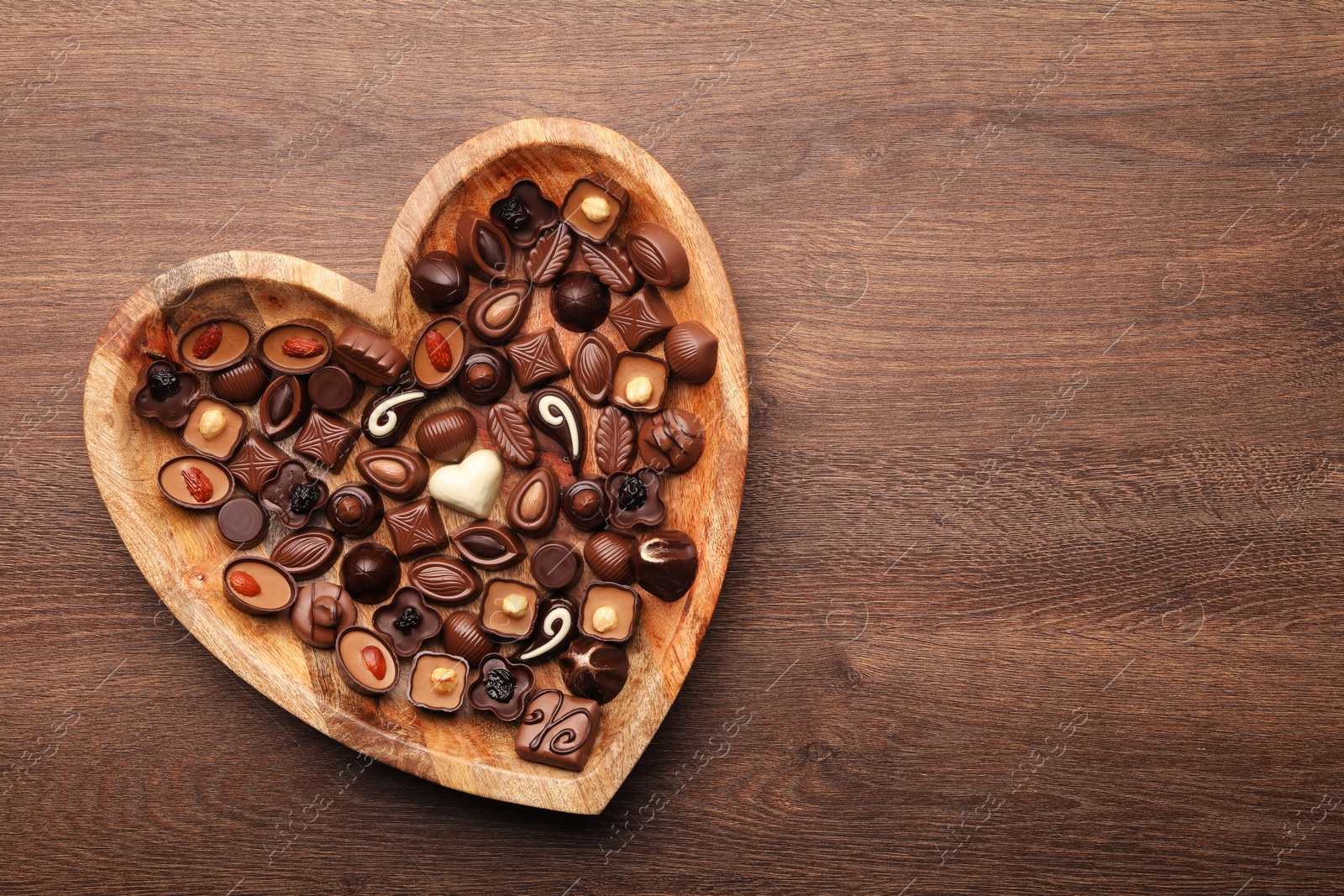 Photo of Heart shaped plate with delicious chocolate candies on wooden table, top view. Space for text