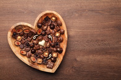 Heart shaped plate with delicious chocolate candies on wooden table, top view. Space for text