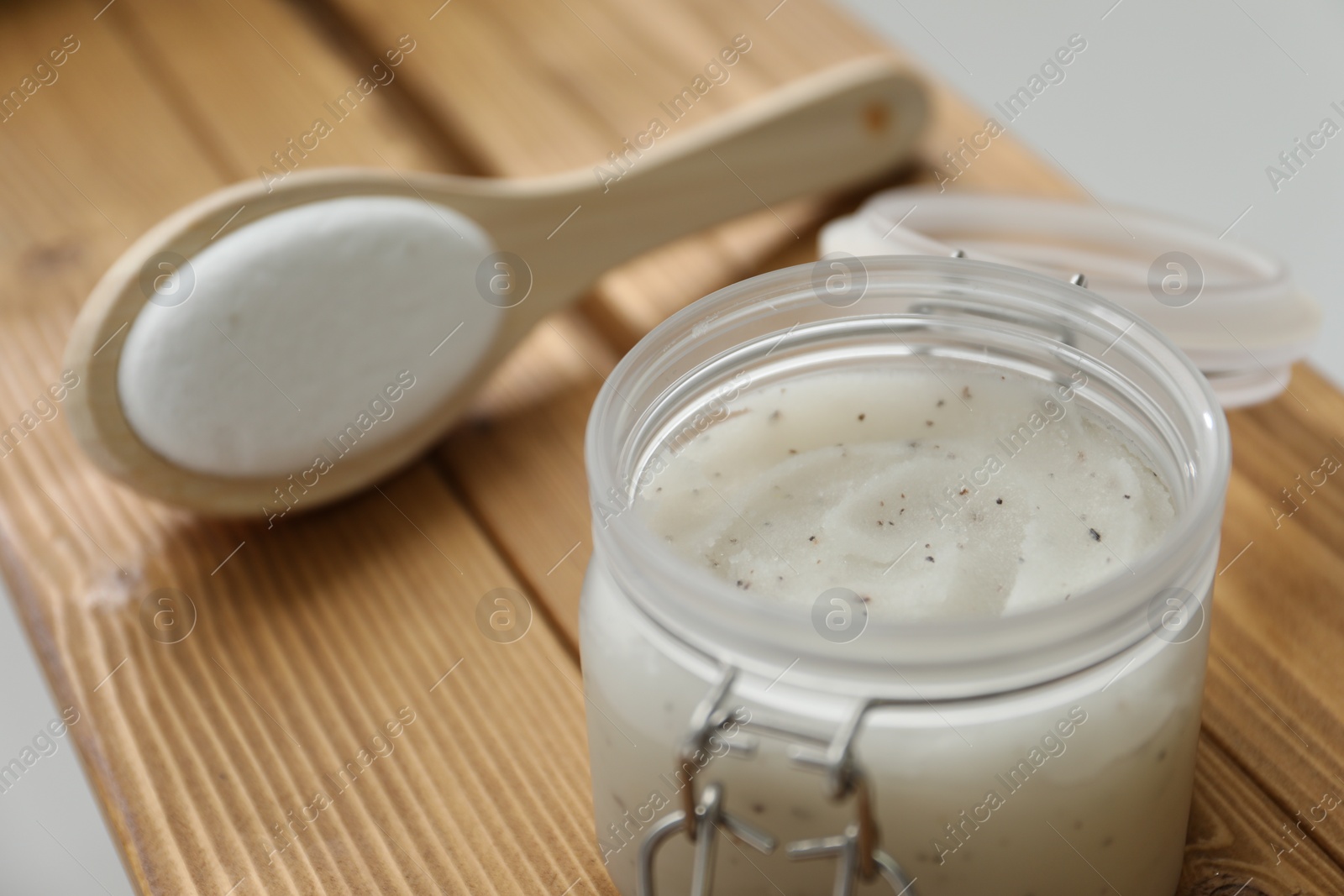 Photo of Wooden tray with scrub in jar and brush on bath tub, closeup