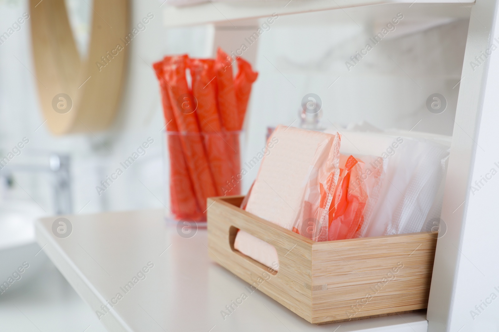 Photo of Organizer with tampons and menstrual pads on shelving unit in bathroom. Feminine hygiene products