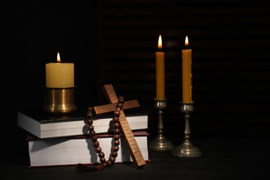 Church candles, Bible, rosary beads and cross on wooden table in darkness