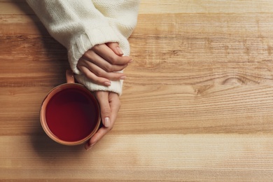 Photo of Woman holding cup of tea at wooden table, top view. Space for text