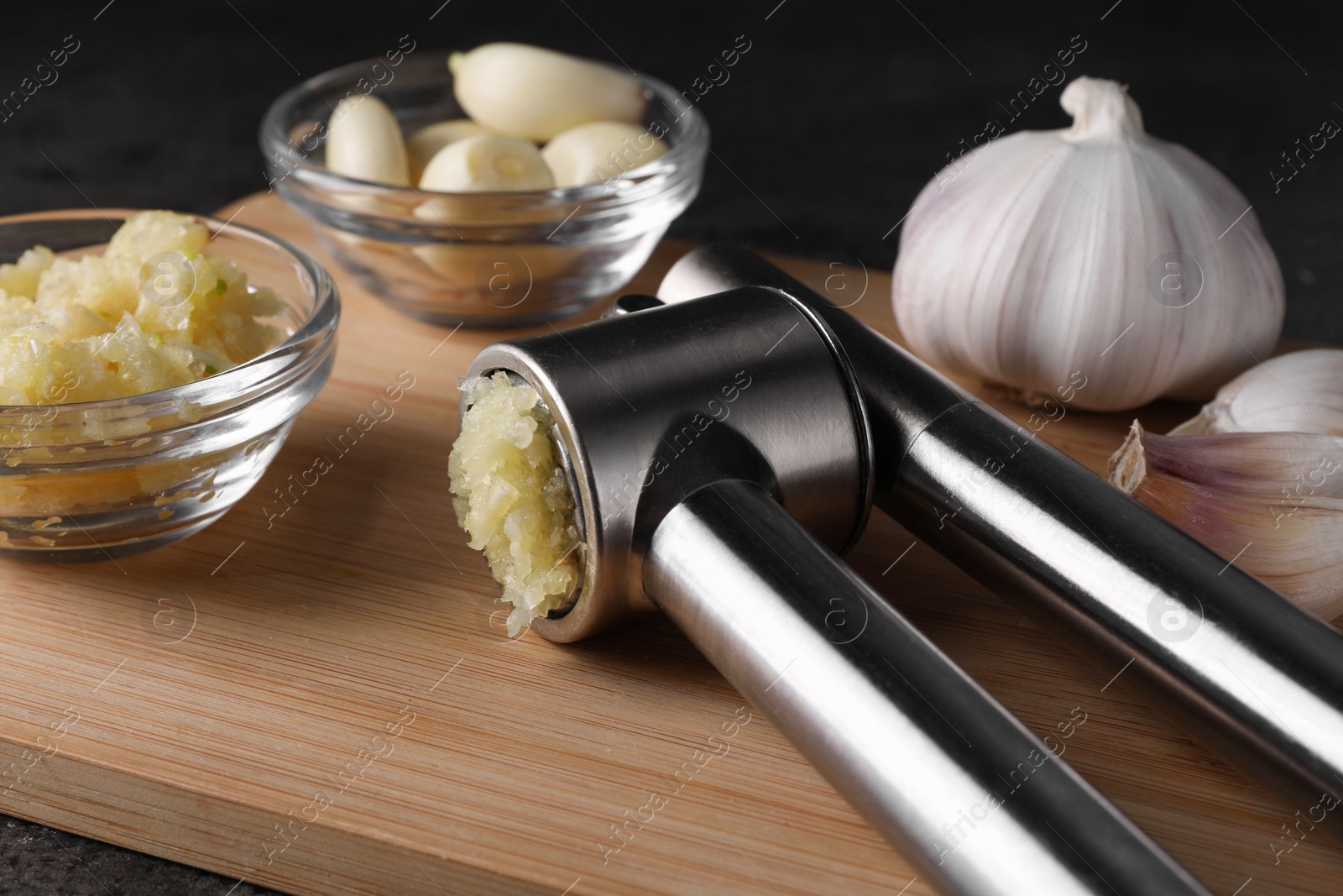 Photo of Garlic press, cloves and mince on wooden table, closeup