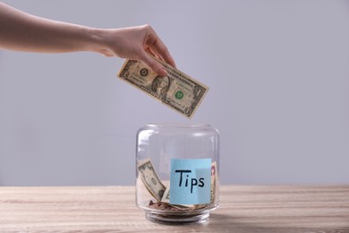 Woman putting tips into glass vase on wooden table, closeup